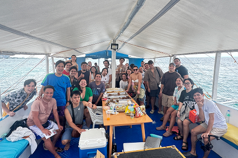 A large team enjoying a boat outing and gathering around a table with food.