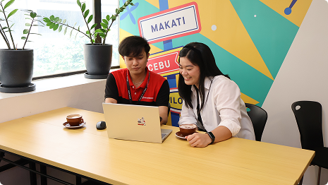 Team members working together at a laptop in a bright, casual workplace.